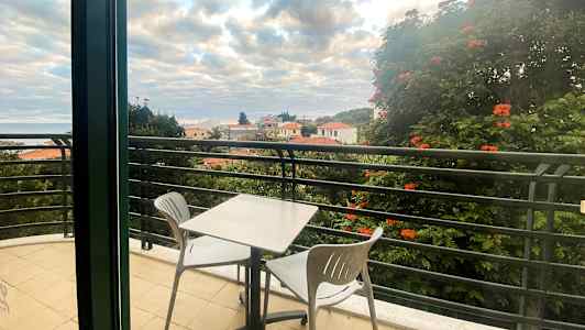 Parveke, jossa pöytä ja kaksi tuolia, näkymä kattotörmiin ja puihin. (Tekoälyn luoma teksti)