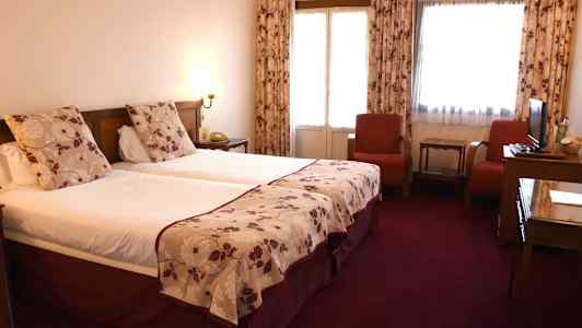 Kahden hengen huone, jossa kaksi erillistä vuodetta, punaiset tuolit ja pöytä. (Tekoälyn luoma teksti)