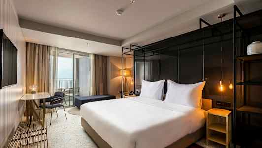 Hotellihuone, jossa on parivuode, pöytä ja tuolit sekä parveke. (Tekoälyn luoma teksti)