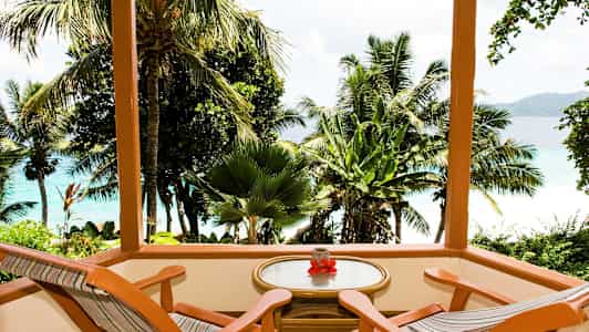 Puuterassi, jossa on kaksi tuolia ja pöytä, jolta avautuu näkymä trooppisiin palmuihin ja siniseen mereen. (Tekoälyn luoma teksti)