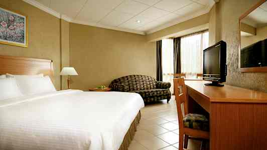 Hotellihuone, jossa suuri sänky, kirjoituspöytä, TV ja sohva. (Tekoälyn luoma teksti)