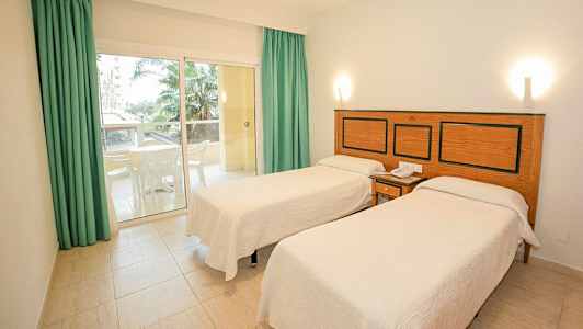 Hotellihuone, jossa kaksi erillistä vuodetta, pieni patio kalusteilla ja näkymä palmuihin. (Tekoälyn luoma teksti)