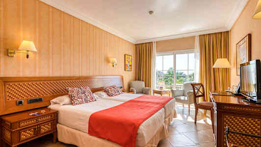 Kuva hotellihuoneesta, jossa on kaksi sänkyä, tuoli ja pöytä sekä televisio. (Tekoälyn luoma teksti)