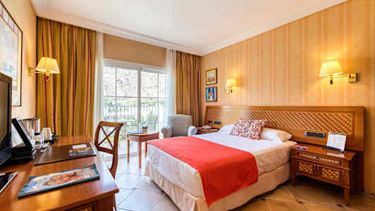 Hotellihuone, jossa on sänky, yöpöytä, kirjoituspöytä ja nojatuoli ikkunan vieressä. (Tekoälyn luoma teksti)