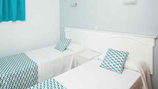 Kaksi yhden hengen sänkyä, joissa on valkoiset vuodevaatteet ja kuvioidut tyynyt ja peitot. (Tekoälyn luoma teksti)