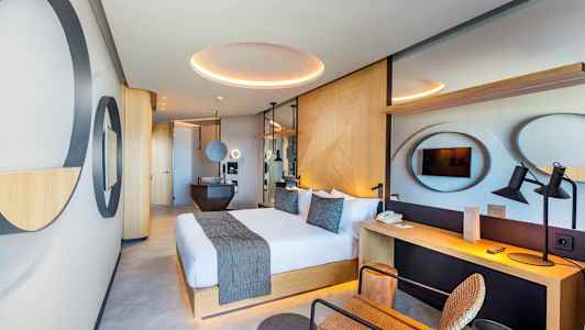 Moderni hotellihuone, jossa suuri parisänky, työpöytä ja TV. (Tekoälyn luoma teksti)