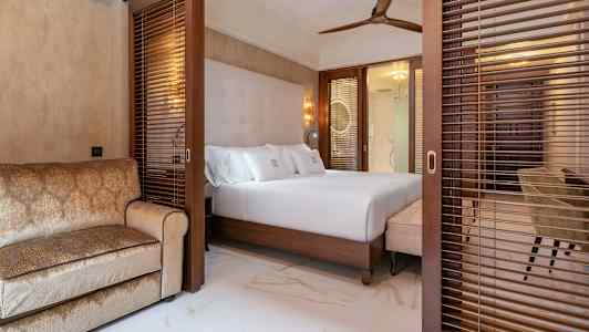 Hotellihuone, jossa on parisänky ja sohva, erotettu puusälekaihtimilla. (Tekoälyn luoma teksti)