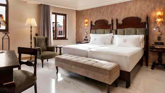 Huone, jossa on kaksi sänkyä, istuinalue ja ikkunoita. (Tekoälyn luoma teksti)