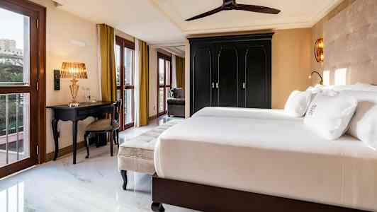 Hotellihuone, jossa parivuode, musta kaappi, kultainen pöytälamppu ja ikkunat kultaverhoilla. (Tekoälyn luoma teksti)