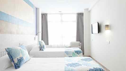 Kaksi erillistä vuodetta, joissa on siniset ja valkoiset vuodevaatteet, valoisassa huoneessa, jossa on suuri ikkuna. (Tekoälyn luoma teksti)