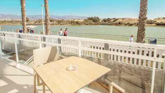 Näkymä terassilta, jolla on pöytä ja tuoli. Taustalla näkyy vettä ja kävelytie. (Tekoälyn luoma teksti)