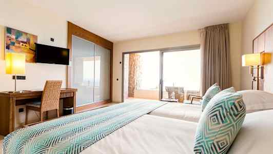 Hotellihuoneen kuva, jossa on kaksi vuodetta, työpöytä, televisio ja parveke tuoleineen. (Tekoälyn luoma teksti)