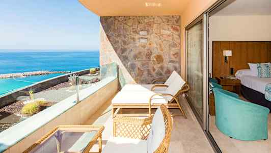 Terassi, jolla on aurinkotuoleja, pöytä ja merinäköala, hotellihuoneen vieressä. (Tekoälyn luoma teksti)