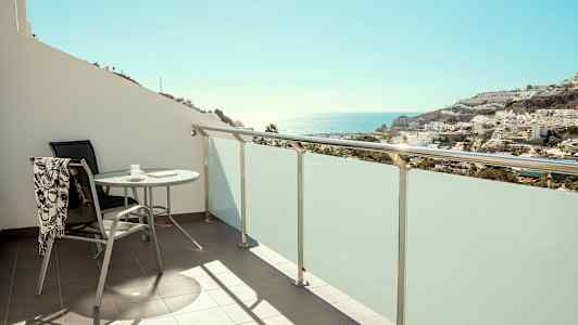 Parveke, jossa pöytä ja tuoli, näkymä merelle ja rakennuksiin. (Tekoälyn luoma teksti)