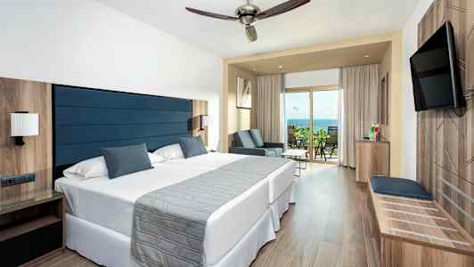 Hotellihuone, jossa on kaksi sänkyä, oleskelualue ja parveke merinäköalalla. (Tekoälyn luoma teksti)