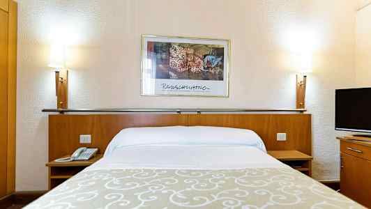 Hotellisänky valkoisilla lakanoilla, beige koriste, kaksi sängyn lamppua ja seinämaalaus taustalla. (Tekoälyn luoma teksti)