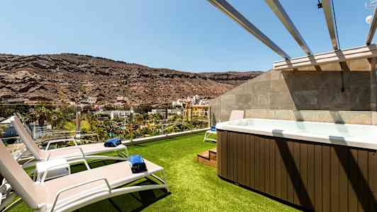 Kuva terassista, jossa on nurmipintaa, aurinkotuoleja ja poreallas vuoristomaiseman äärellä. (Tekoälyn luoma teksti)