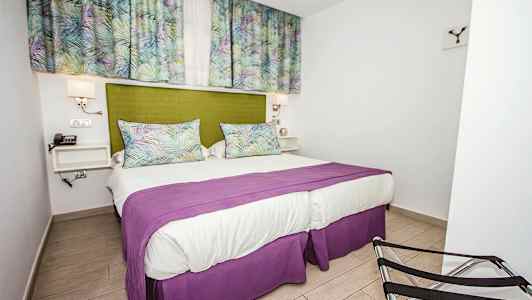 Makuuhuone, jossa on parivuode, vihreä sängynpääty, violetti päiväpeite ja kuvioidut verhot. (Tekoälyn luoma teksti)