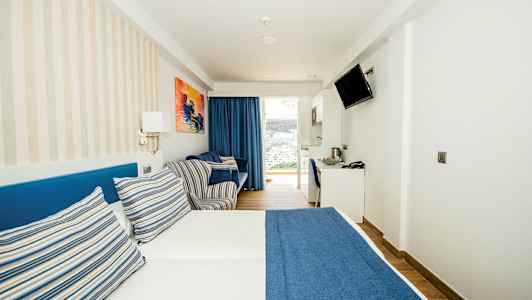 Hotellihuone, jossa on parisänky sinisellä päiväpeitteellä ja raidallisilla tyynyillä. (Tekoälyn luoma teksti)