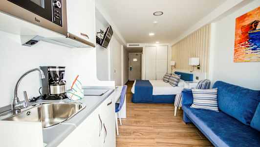 Hotellihuone, jossa on sänky, sininen sohva ja keittokomero pesualtaalla. (Tekoälyn luoma teksti)