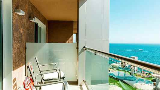 Parveke, jossa kaksi tuolia, lasikaide ja näkymä merelle. (Tekoälyn luoma teksti)