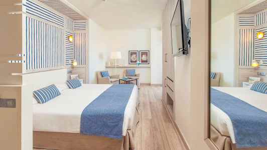 Hotellihuone, jossa on parivuode ja tuoli, sisustettu vaalealla ja modernilla tyylillä. (Tekoälyn luoma teksti)