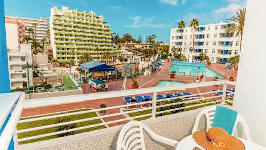 Näkymä parvekkeelta hotellialueelle, jossa on uima-allas ja aurinkotuolit sekä rakennuksia taustalla. (Tekoälyn luoma teksti)