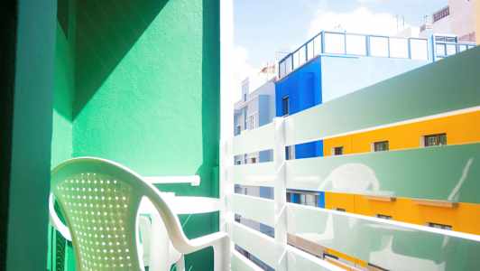 Parveke vihreällä seinällä, valkoinen muovituoli ja näköala värikkäisiin rakennuksiin. (Tekoälyn luoma teksti)