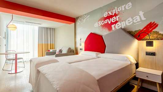 Moderni hotellihuone, jossa on kaksi yhden hengen vuodetta ja värikkäitä yksityiskohtia. (Tekoälyn luoma teksti)