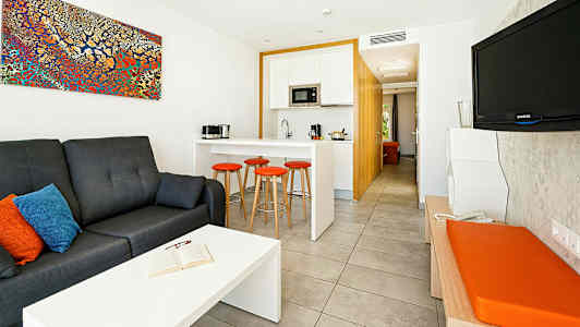 Moderni hotellihuone, jossa on istuinryhmä, keittiö ja televisio. (Tekoälyn luoma teksti)