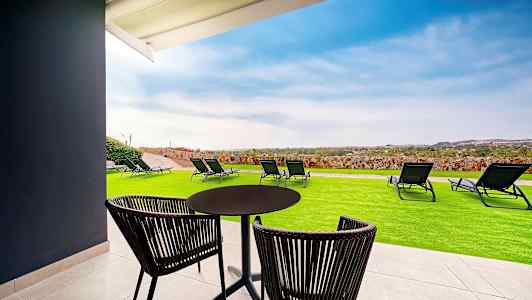 Terassi, jossa pöytä, tuolit, nurmikko ja aurinkotuoleja, näkymä maisemaan. (Tekoälyn luoma teksti)