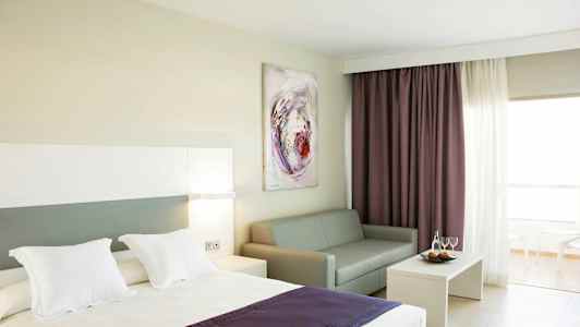 Hotellihuone, jossa sänky, sohva, sohvapöytä ja verhot. (Tekoälyn luoma teksti)