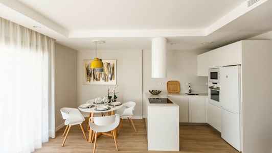 Moderni keittiö ruokailutiloineen, valkoisia kalusteita ja vaalea sisustus. (Tekoälyn luoma teksti)