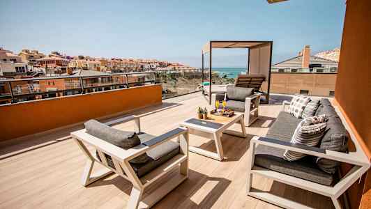 Tilava terassi, jossa on istuimia ja pöytiä, näkymät merelle ja ympäröiviin rakennuksiin. (Tekoälyn luoma teksti)