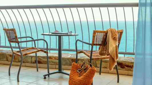 Merinäkymä parvekkeelta, jossa on pöytä, kaksi tuolia ja rantakassi. (Tekoälyn luoma teksti)