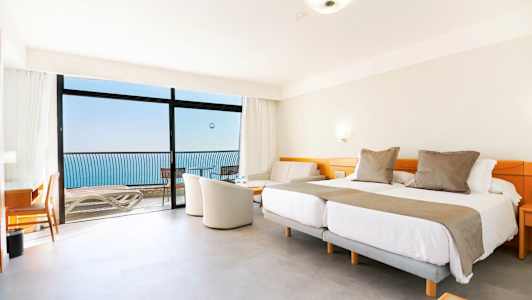 Hotellihuone, jossa on parivuoteet, istuinryhmä ja parveke merinäköalalla. (Tekoälyn luoma teksti)