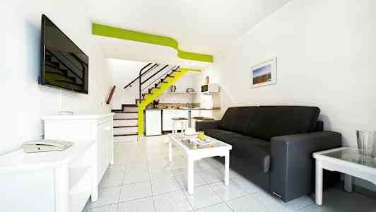 Hotellihuone, jossa sohva, sohvapöytä, televisio ja pieni keittonurkkaus. (Tekoälyn luoma teksti)