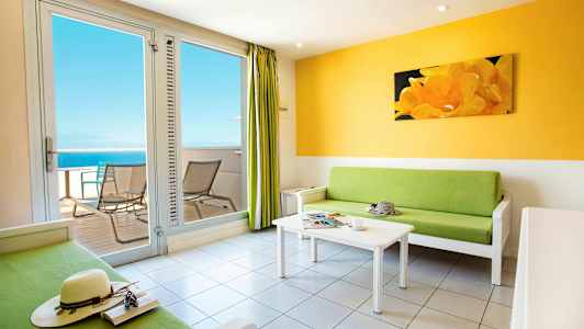 Valoisa olohuone, jossa on vihreä sohva, valkoinen sohvapöytä ja parveke merinäköalalla. (Tekoälyn luoma teksti)