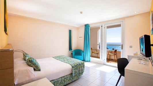 Hotellihuone, jossa on sänky, kirjoituspöytä ja tuoli. Ikkuna merinäköalalla. (Tekoälyn luoma teksti)