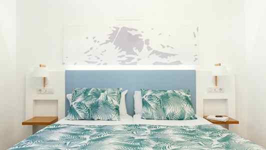 Vuode vihreä-valkoisella kuvioidulla peitolla ja tyynyillä, sininen sängynpääty ja valkoiset seinät. (Tekoälyn luoma teksti)