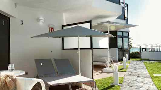 Ulkotila, jossa kaksi aurinkotuolia ja aurinkovarjoja rakennuksen luona. (Tekoälyn luoma teksti)