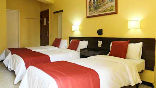 Hotellihuone, jossa kaksi yhden hengen sänkyä, valkoiset lakanat ja punaiset koristeelliset päiväpeitot. (Tekoälyn luoma teksti)