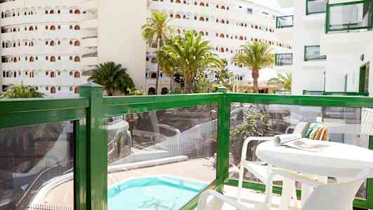 Parveke pöydän ja tuolien kera, näkymä uima-altaalle ja ympäröiviin rakennuksiin. (Tekoälyn luoma teksti)