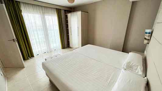 Hotellihuone, jossa on suuri sänky, vaatekaappi ja ikkuna verhoilla. (Tekoälyn luoma teksti)