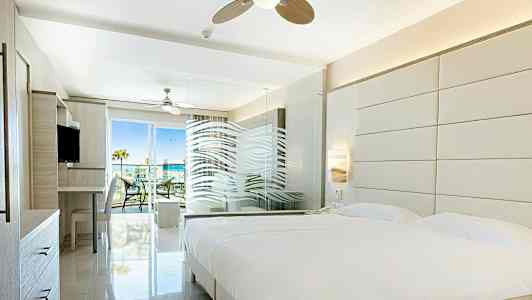 Valoisa hotellihuone, jossa suuri sänky, lasiseinä ja pääsy parvekkeelle. (Tekoälyn luoma teksti)