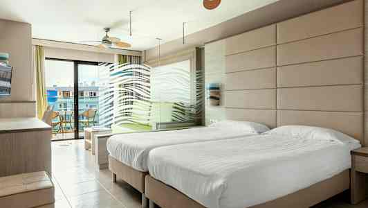 Hotellihuone, jossa on kaksi yhden hengen vuodetta, istuinryhmä ja parveke näkymällä. (Tekoälyn luoma teksti)