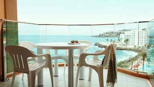 Näkymä parvekkeelta, jossa on pöytä ja muovituoleja, meri ja rakennuksia taustalla näkyvissä. (Tekoälyn luoma teksti)