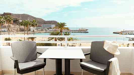 Kaksi tuolia ja pöytä parvekkeella, josta on näkymä rannalle ja merelle. (Tekoälyn luoma teksti)