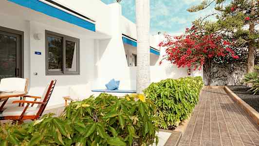 Terassi, jossa istuimia, valkoisen rakennuksen edessä, jossa sinisiä yksityiskohtia. (Tekoälyn luoma teksti)