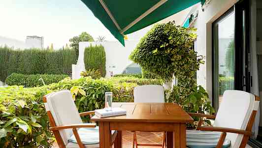 Ulkokalusteet, joihin kuuluu kolme tuolia pöydän ympärillä terassilla, ympäröitynä vihreillä kasveilla. (Tekoälyn luoma teksti)